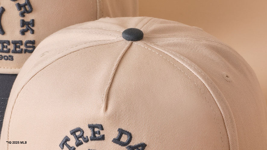 A detail image of the top blue button on a cream hat. There is also matching blue embroidery.