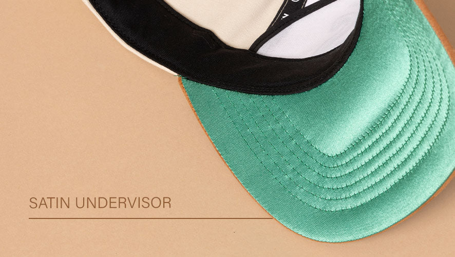Close-up of a cap flipped upward to reveal a bright green satin undervisor with tan and black brim accents.