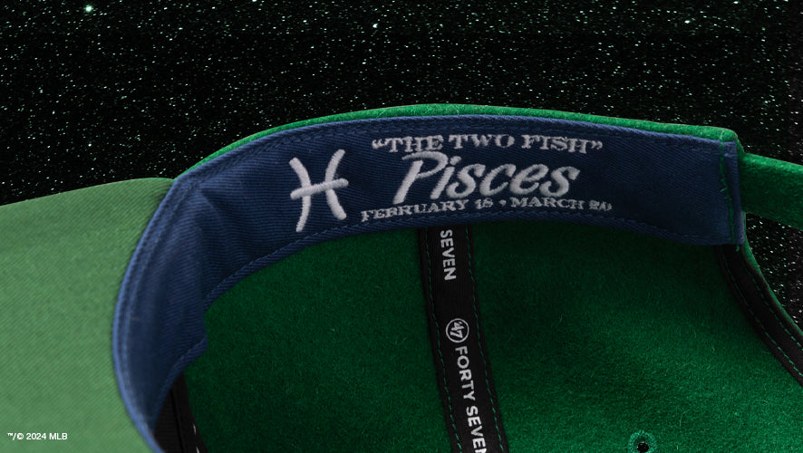 Interior of a green wool cap featuring the Pisces zodiac sign, dates, and “The Two Fish” stitched on the sweatband, part of the Zodiac Collection.