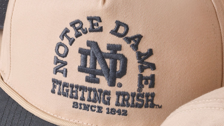 Blue NOTRE DAME FIGHTING IRISH SINCE 1842 embroidery on a cream colored hat with a blue visor.