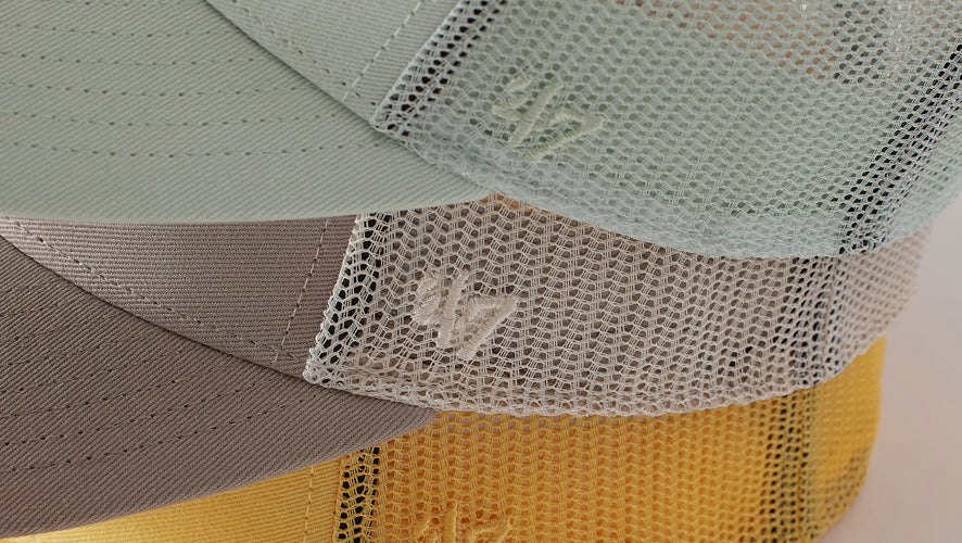 Green, grey and yellow trucker hats with mesh back and '47 logo on the side stacked on top of each other.