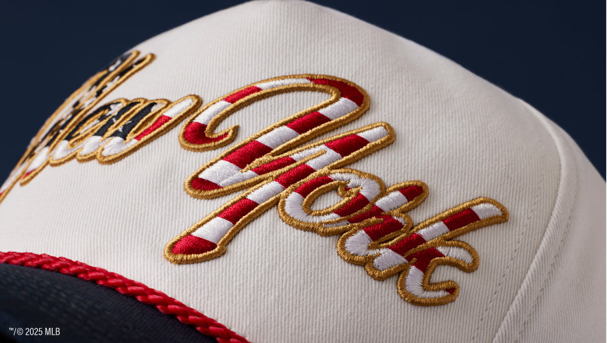 A detailed imagine of the front of a hat with a red rope and a red white and blue New York embroidery with gold outline.