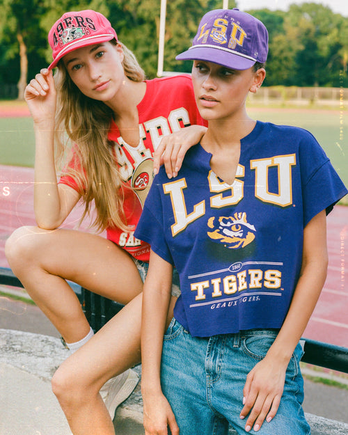 Two women wearing LSU-themed clothing and hats on a track field.