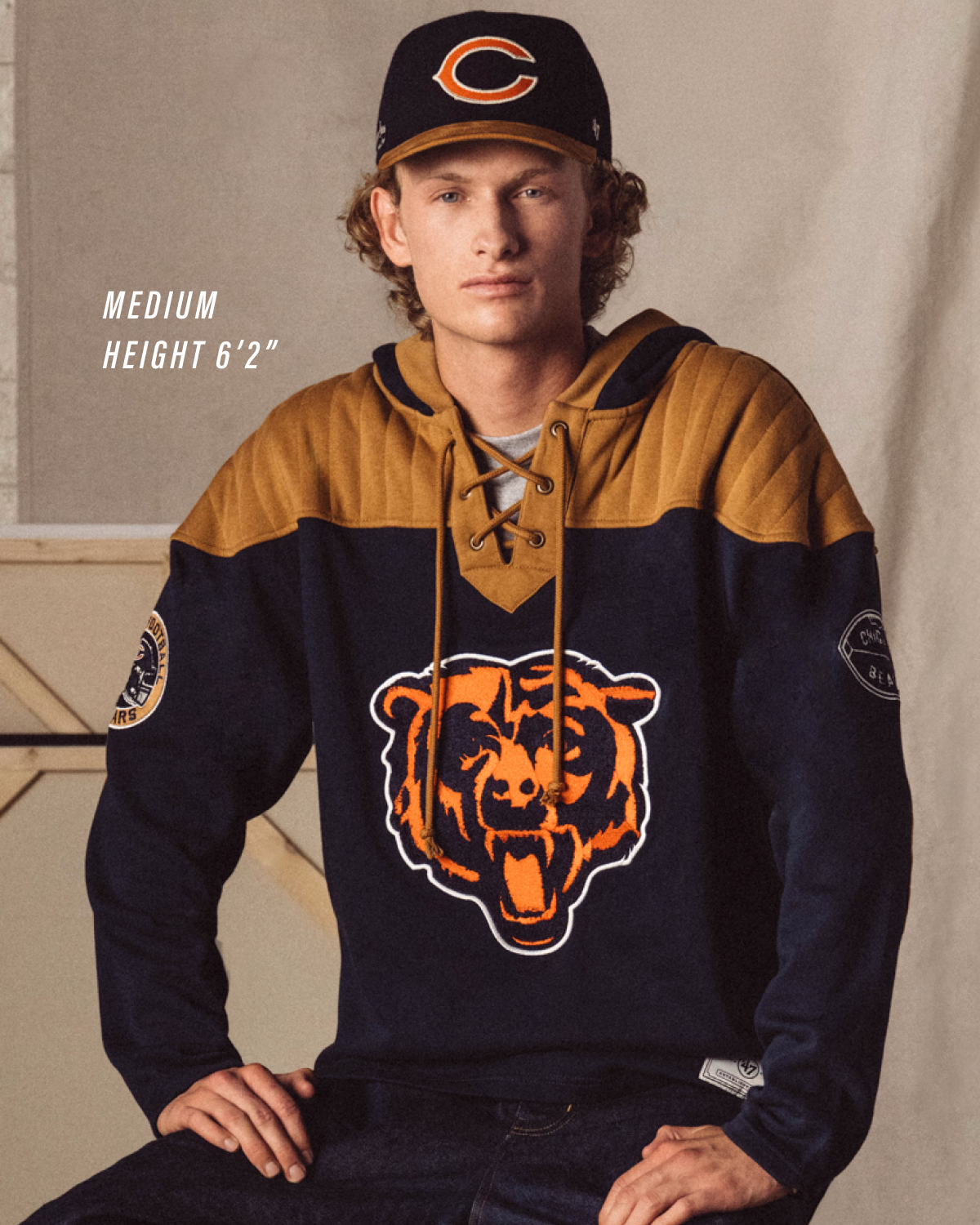 Man wearing a navy and mustard hoodie with a bear logo, sitting against a neutral background.