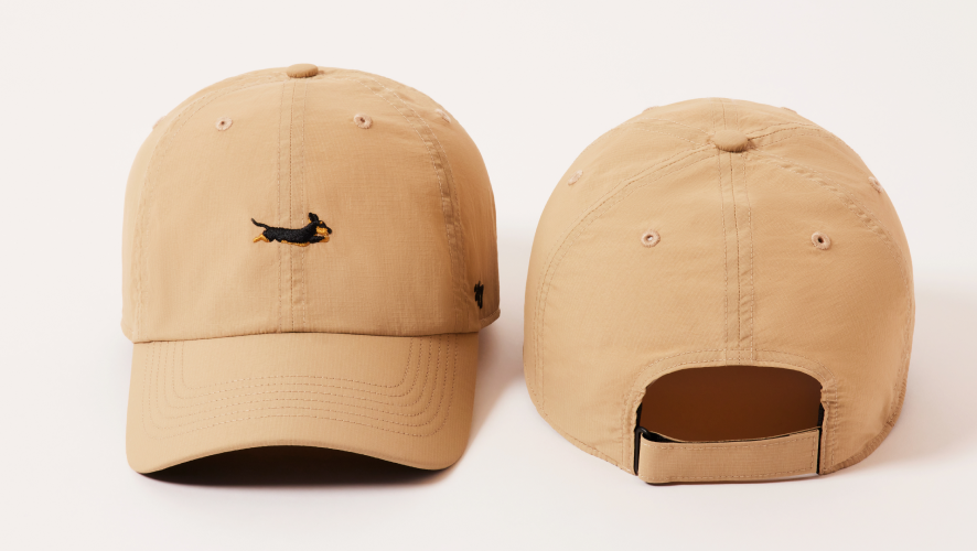 Two beige baseball caps with a small logo on a light pink background