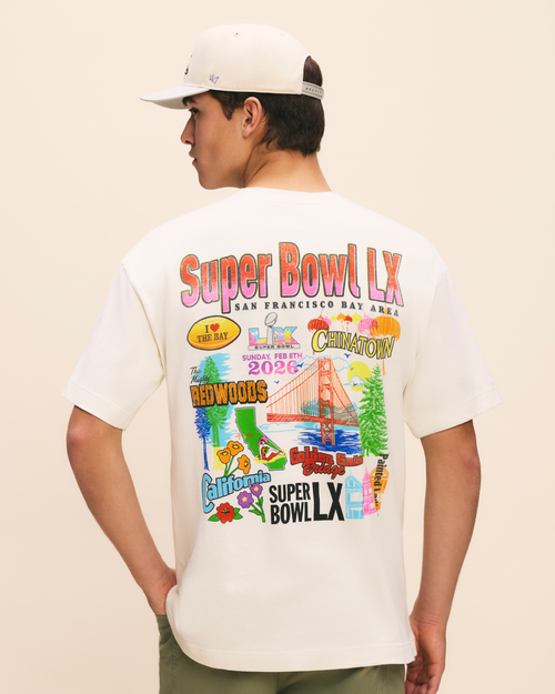 Person wearing a white t-shirt with colorful graphics and text on the back, standing against a beige background.