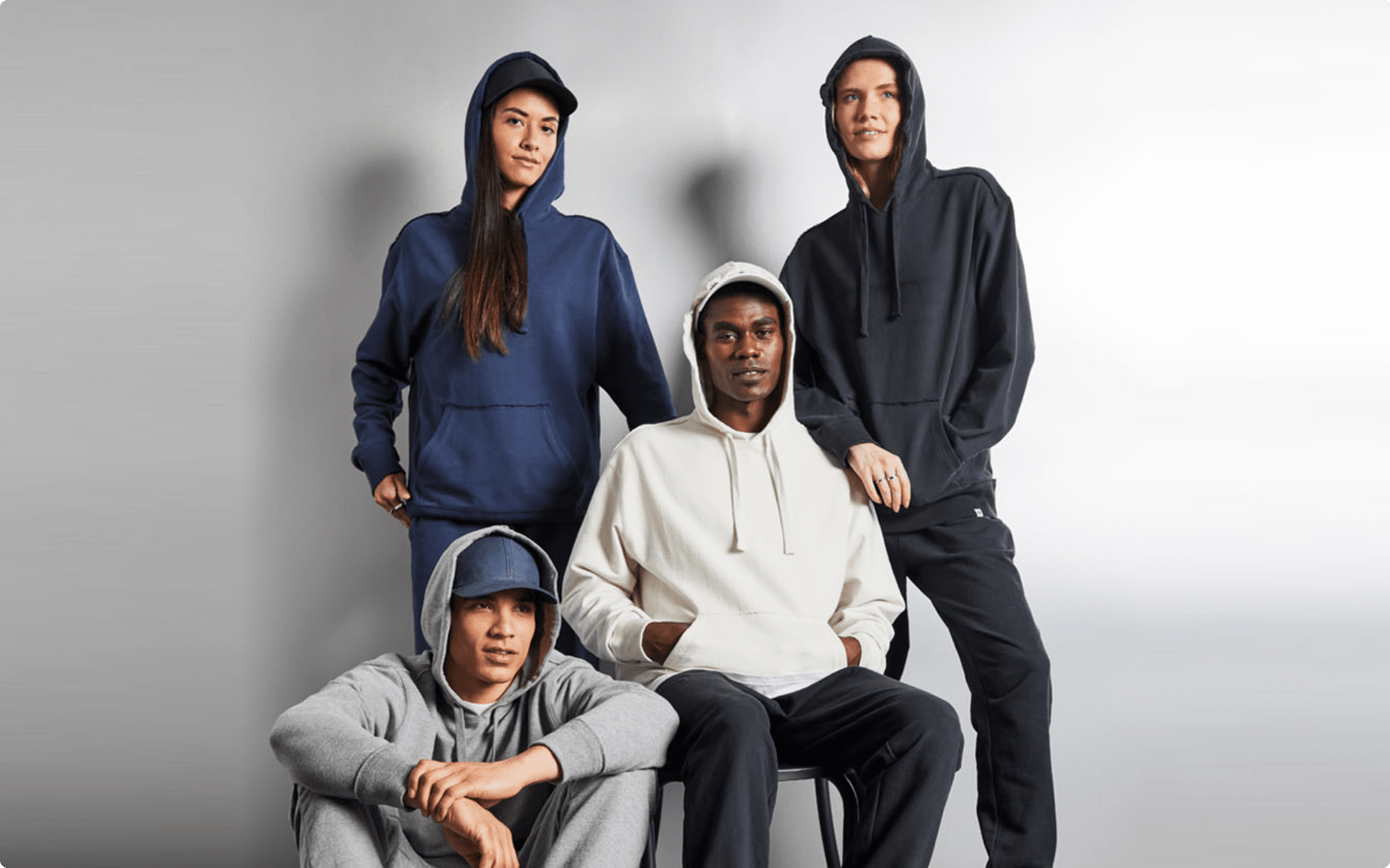 Four models in solid color hoodies and joggers from ‘47 Brand, posed against a light gray background in a casual, modern studio setup.