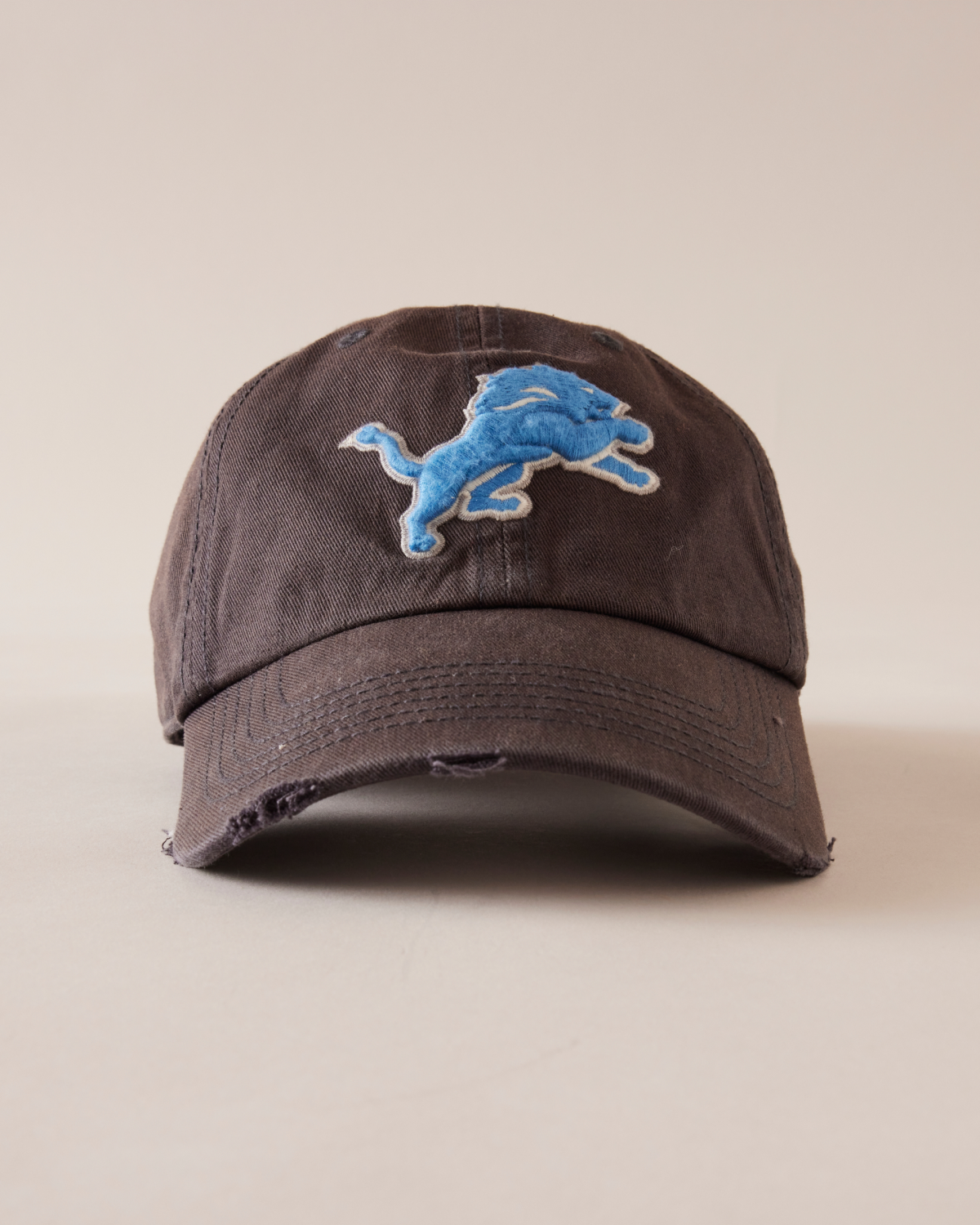 BROWN CAP WITH BLUE LOGO ON A BEIGE BACKGROUND