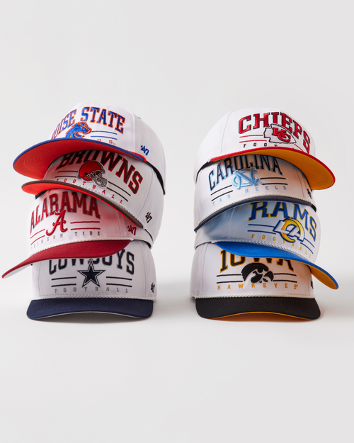 Stack of sports-themed caps with various team logos on a white background
