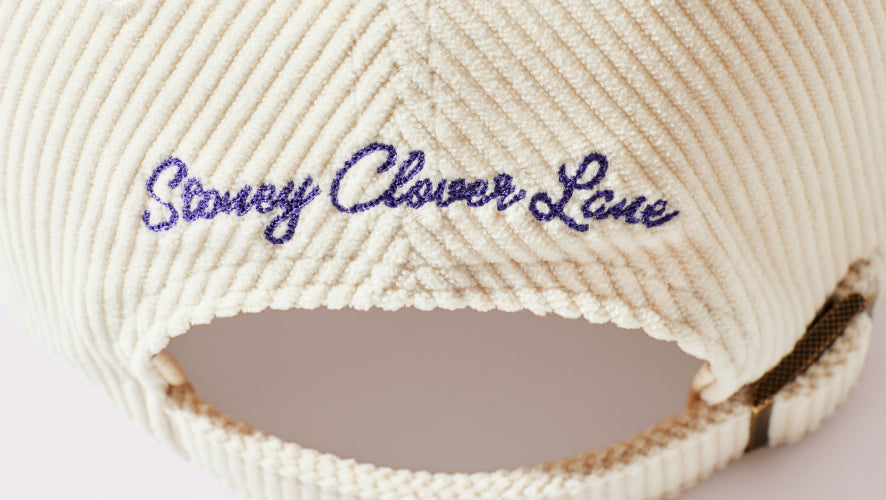 Close-up of a beige woven headband with 'Sleeky Clover Lane' embroidery on a light background