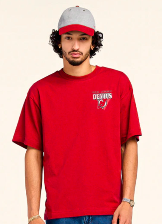 Person wearing a red t-shirt with a logo and a gray and red cap on a beige background