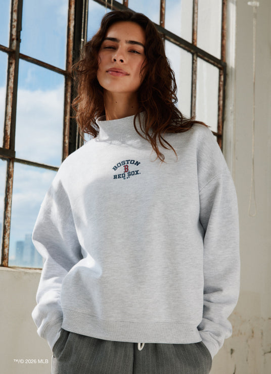 Person wearing a gray sweatshirt with a logo in front of a window