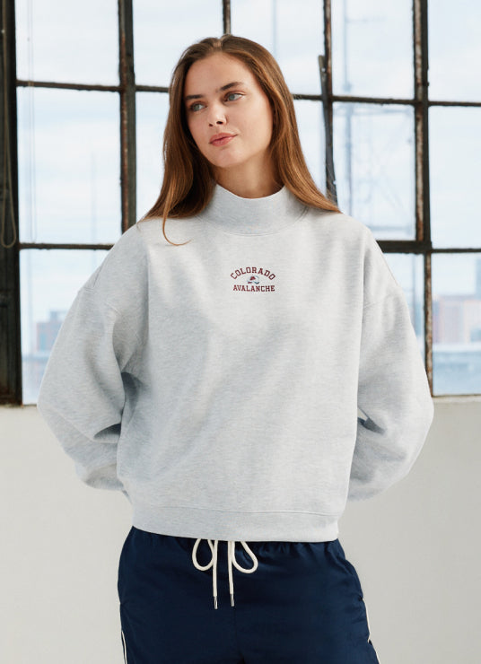 Woman wearing a gray sweatshirt with a logo in front of a window