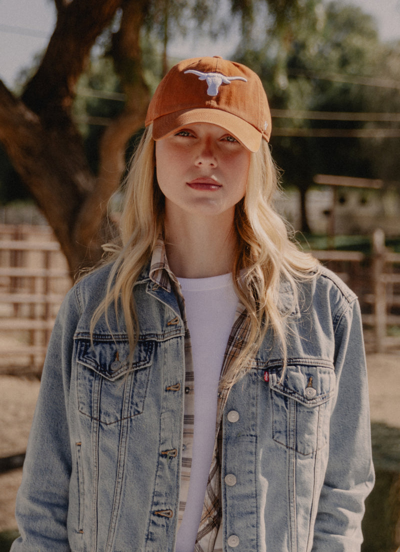 Person wearing an orange cap with a logo and a denim jacket outdoors.