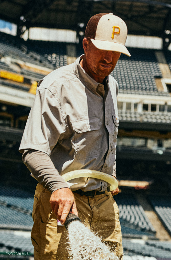 Man watering plants in an empty stadium wearing a cap with a logo.