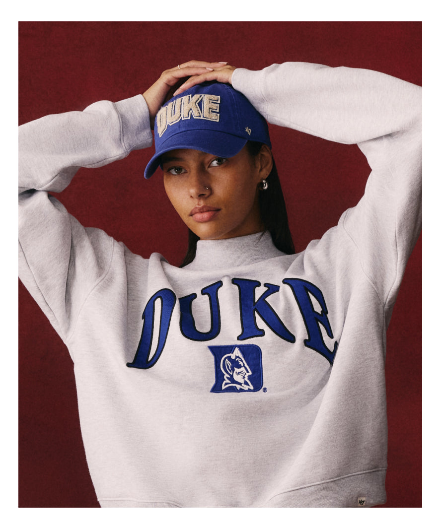 Person wearing a Duke sweatshirt and cap against a red background