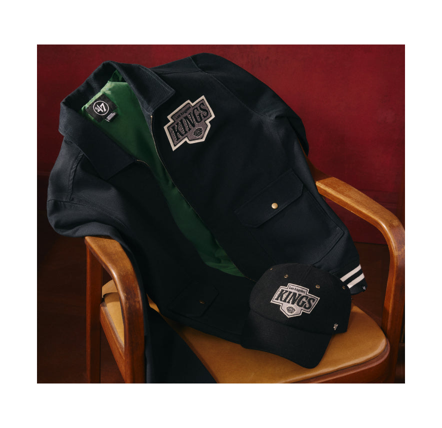 Black jacket and cap with 'KINGS' logo on a wooden chair against a red background