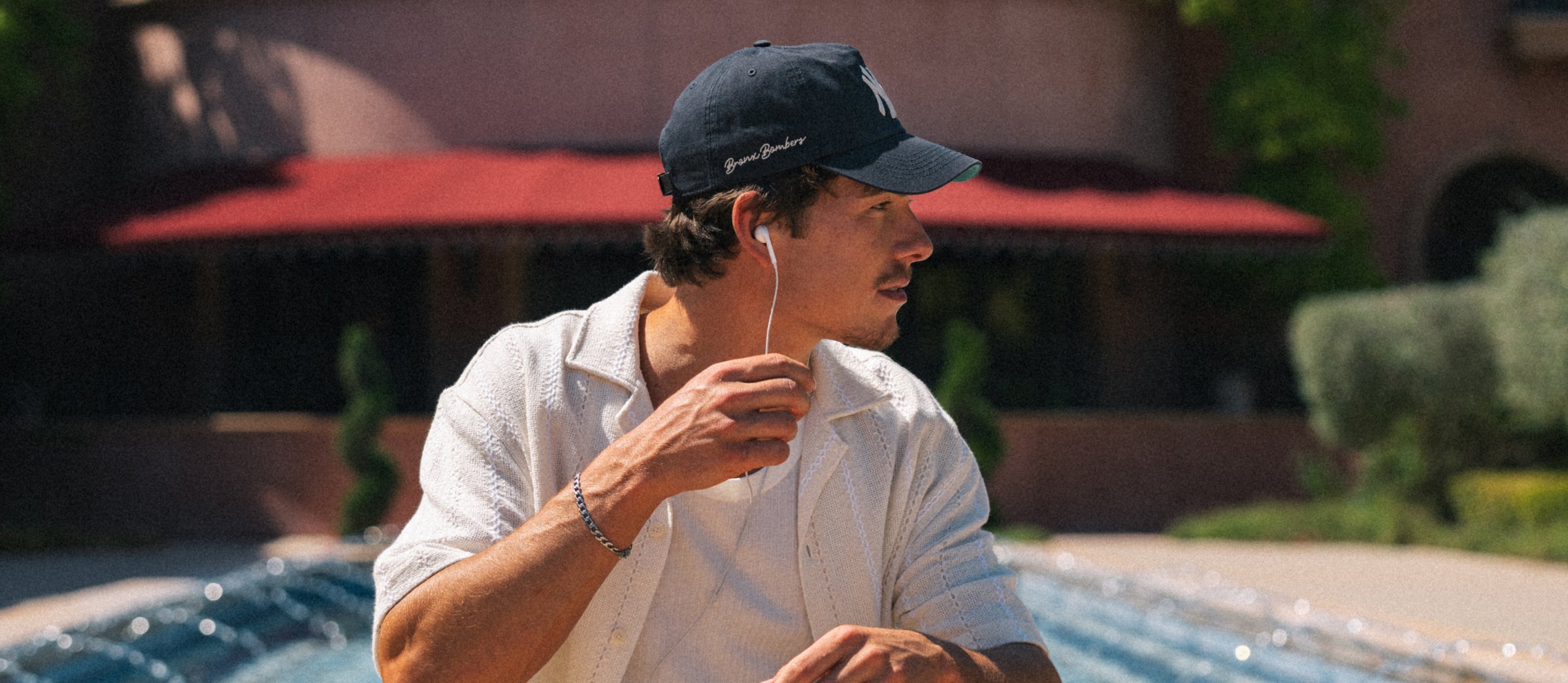 Man by a pool wearing a cap and listening to music with earphones