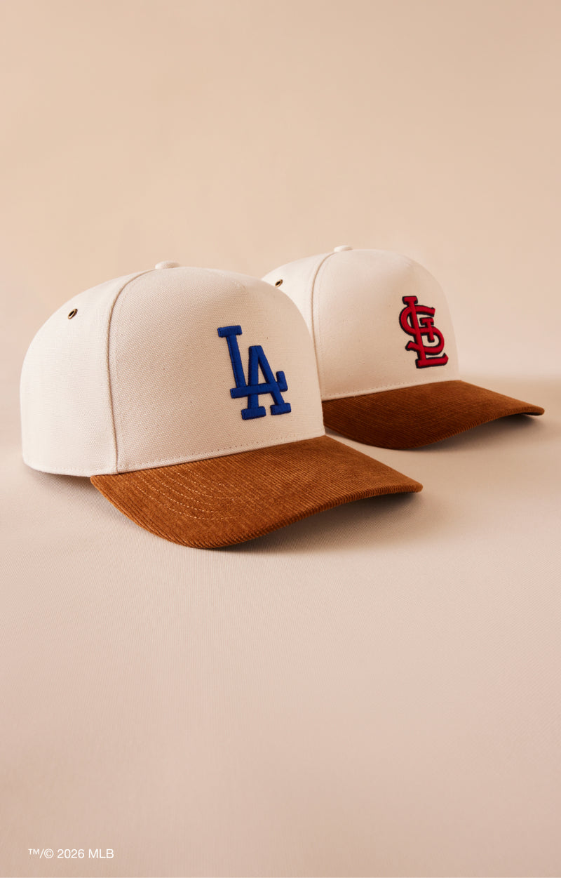 Two baseball caps with LA and STL logos on a beige background