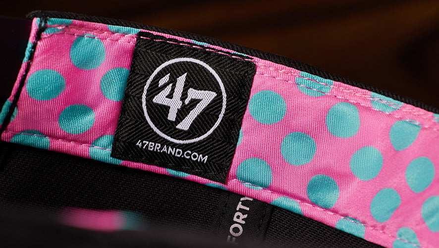A detail image the inside lining of a hat. The linings design is blue polka dots on top of the color pink. it also has a '47 logo on a black label.