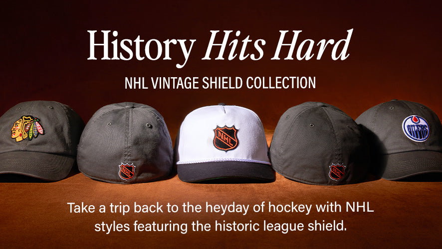 Row of dark-colored NHL caps with retro shield logos, including Blackhawks, Oilers, and a white center cap, shown under warm lighting.