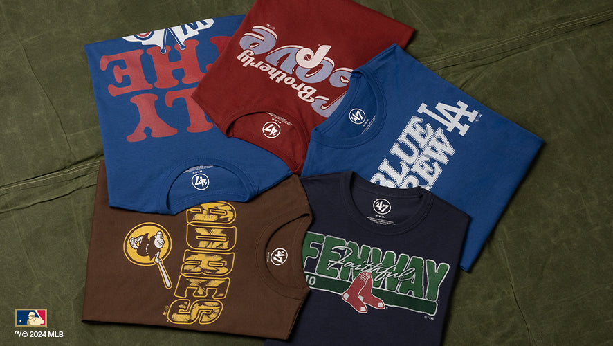 Flat lay of MLB graphic t-shirts in blue, red, brown, and navy, showcasing retro logos for teams like Dodgers, Padres, and Red Sox.