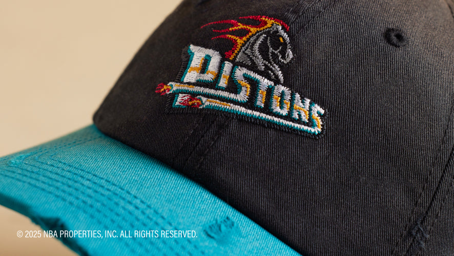 Black cap with 'PISTONS' logo on a beige background