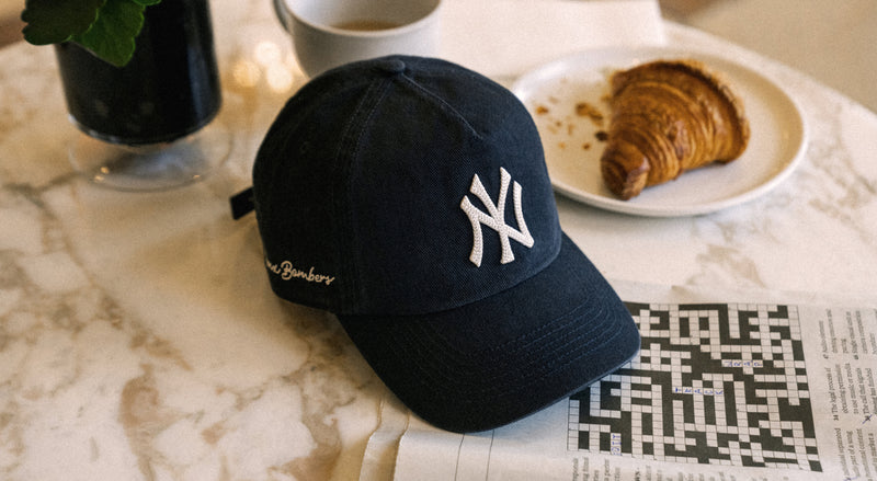 Black cap with a logo on a marble surface with a croissant and coffee.