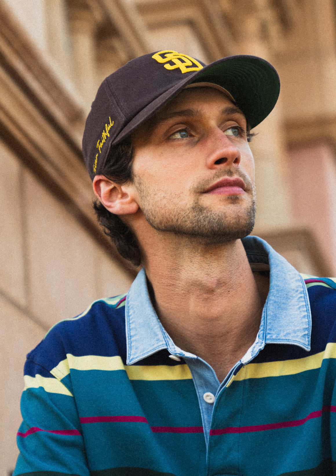 Man wearing a cap and striped shirt with a blurred architectural background