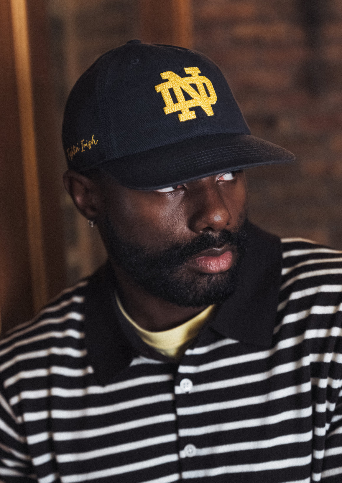 Man wearing a black cap with a yellow logo and a striped shirt.