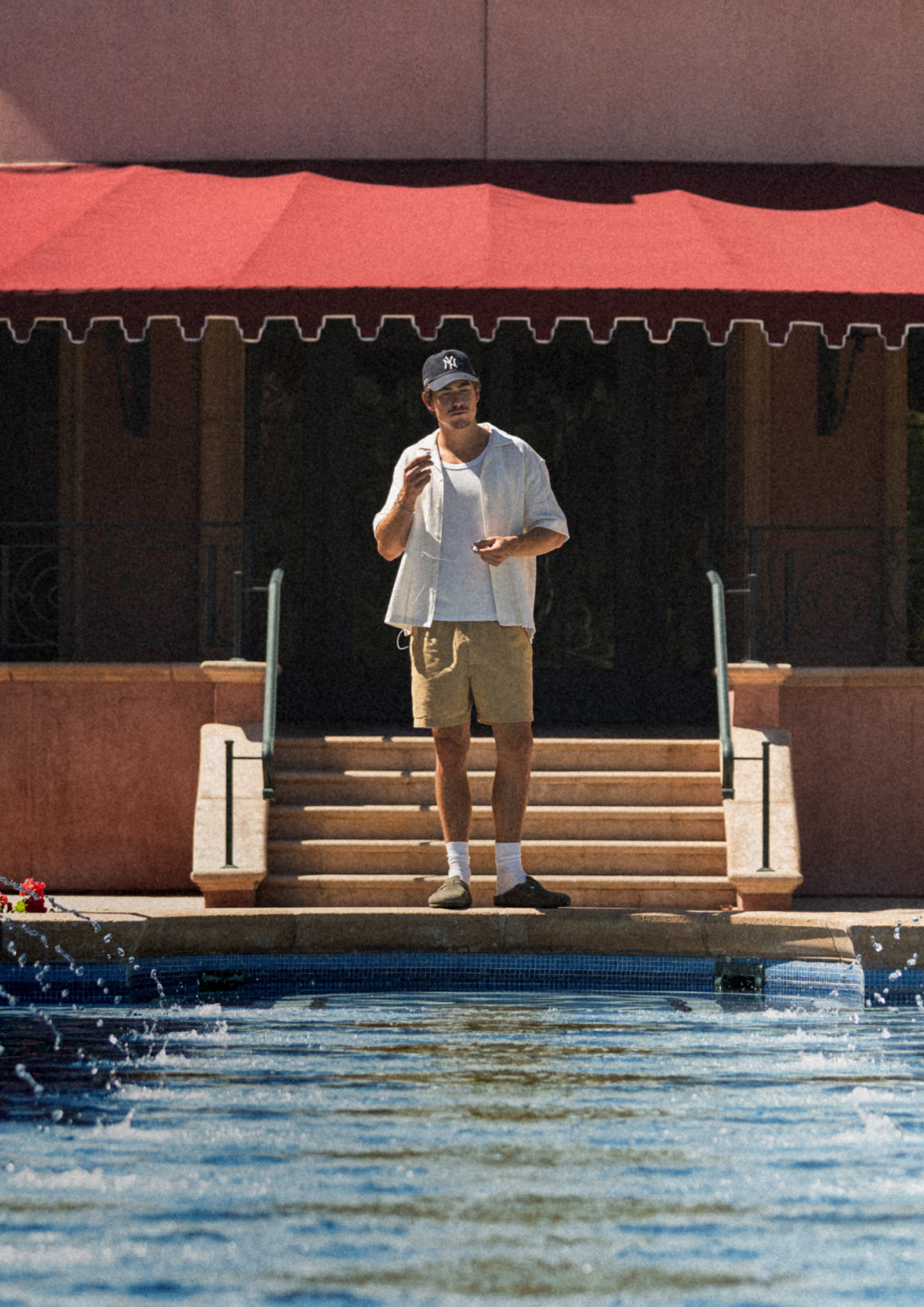 Man standing on steps by a pool with a red awning in the background