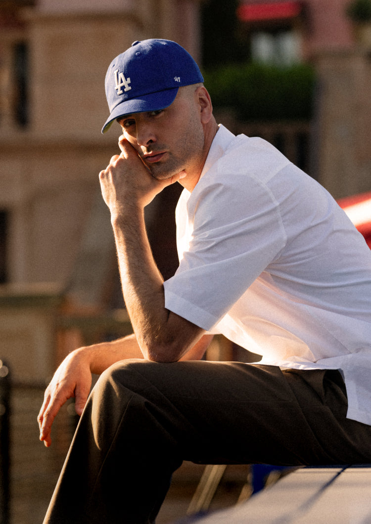 Man wearing a blue cap and white shirt sitting outdoors.