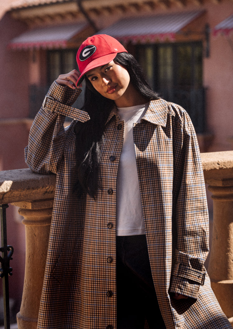 Person wearing a plaid coat and red cap with a logo, standing outdoors.
