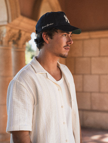 Man wearing a white shirt and dark cap in front of a stone building
