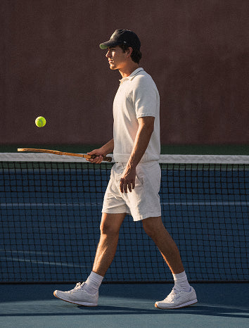 Man playing tennis on a court with a racket and ball.