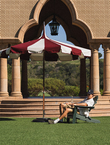 Person sitting under a large red and white umbrella in front of an archway.