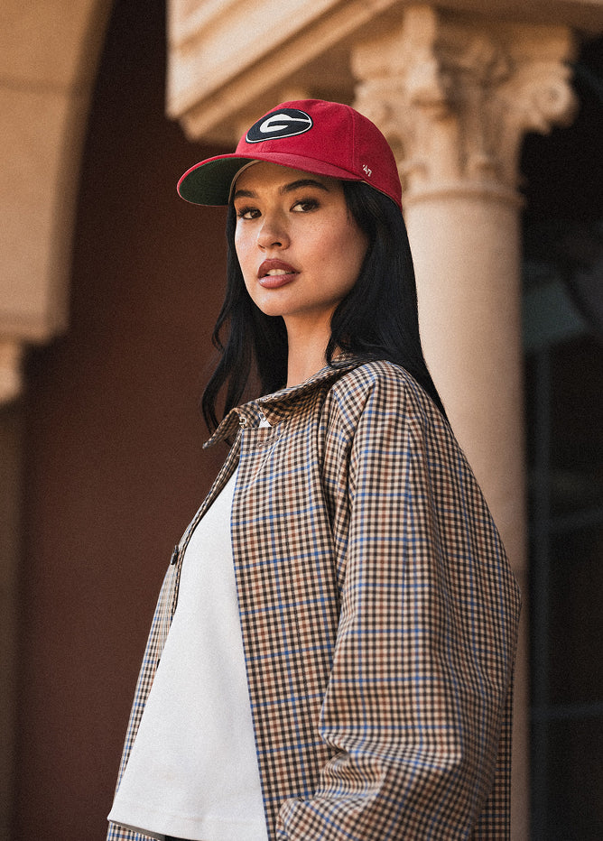 Woman wearing a red cap with a logo and a plaid jacket in an urban setting