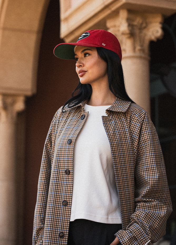 Woman wearing a red cap and checkered jacket standing in front of a building.