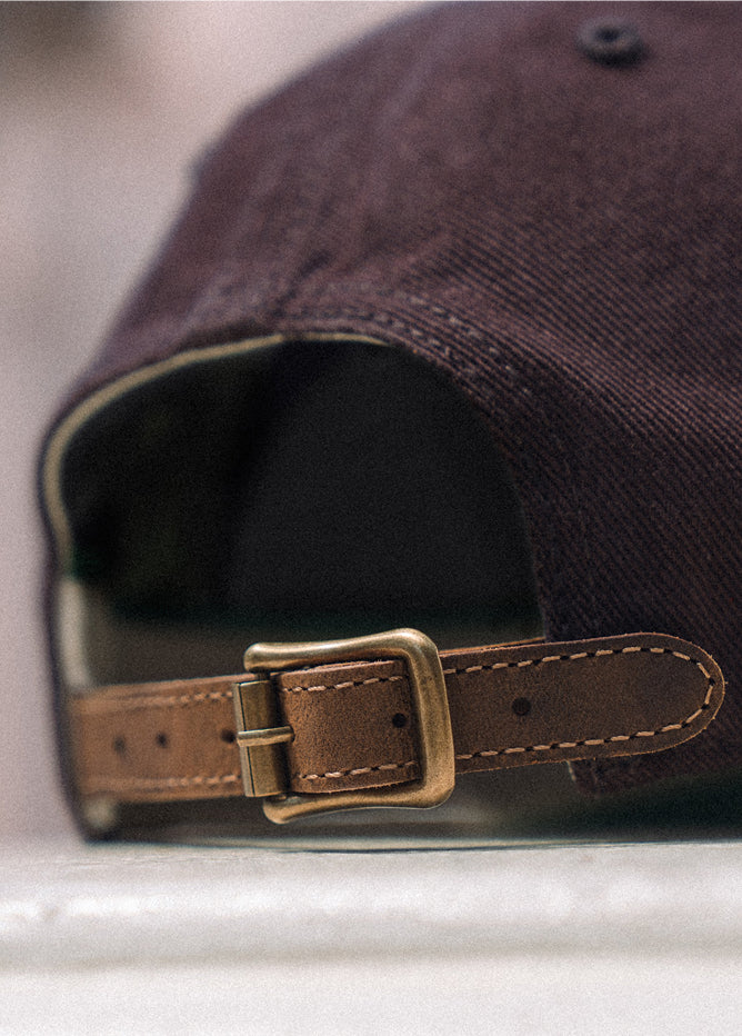 Close-up of a dark-colored cap with a brown leather strap and buckle on a blurred background