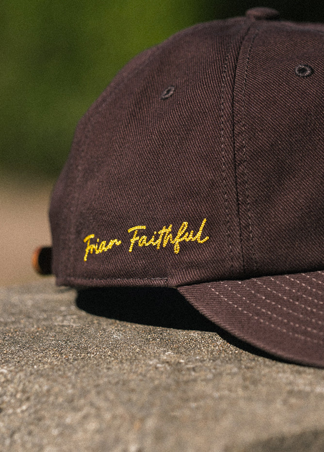 Brown cap with embroidery in yellow on a concrete surface with green grass in the background