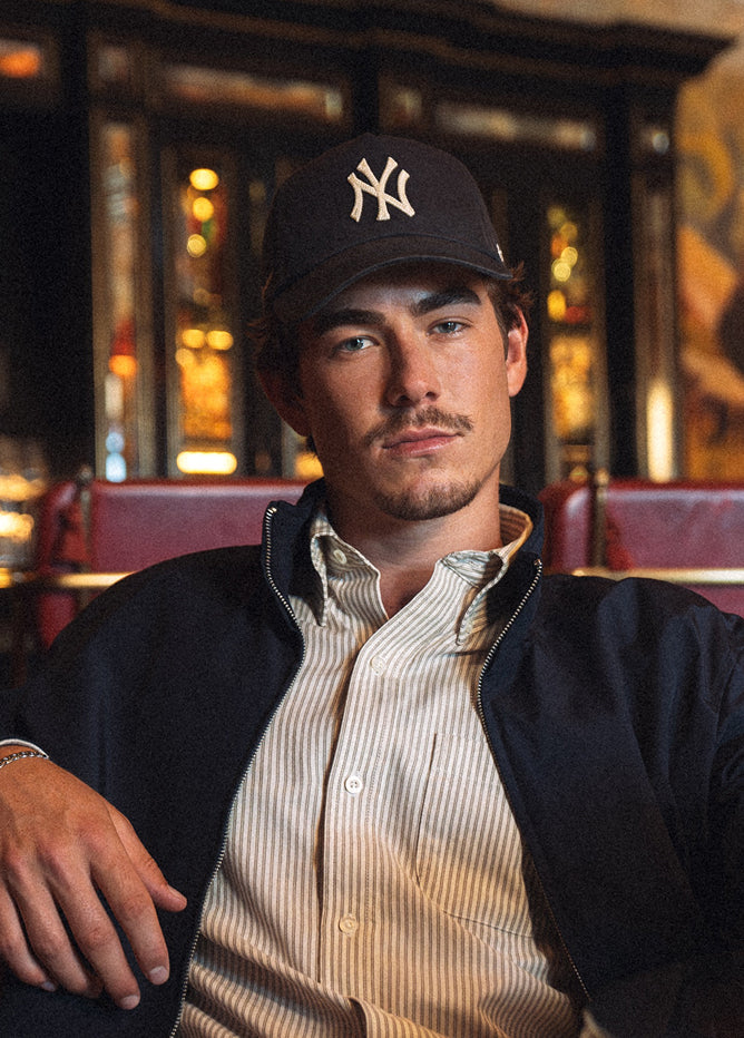 Man wearing a black cap with a logo, sitting in a bar setting.