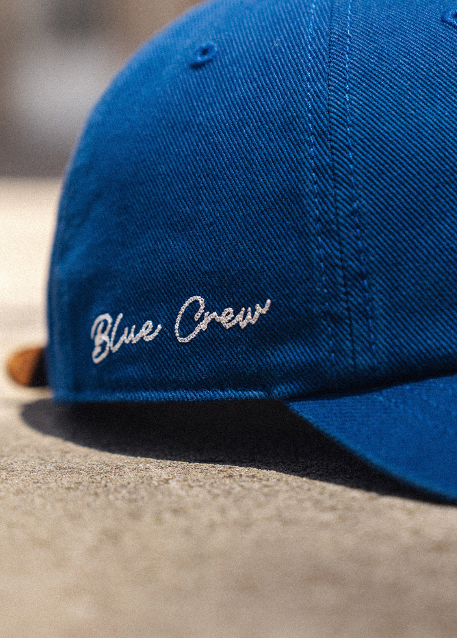 Blue cap with 'Blue Crew' embroidery on a concrete surface