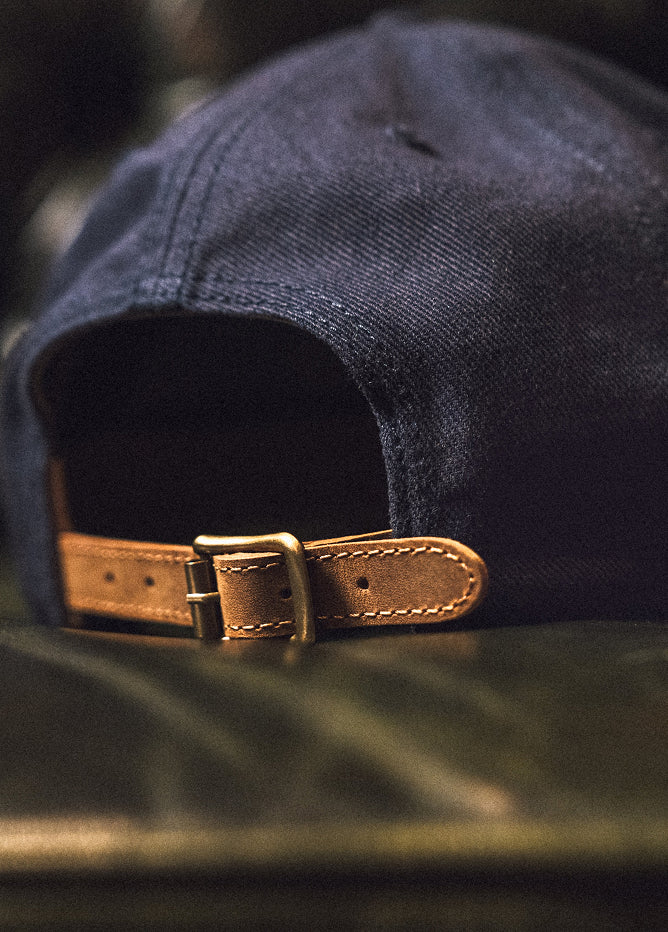 Navy blue cap with a brown leather strap and buckle on a blurred green background