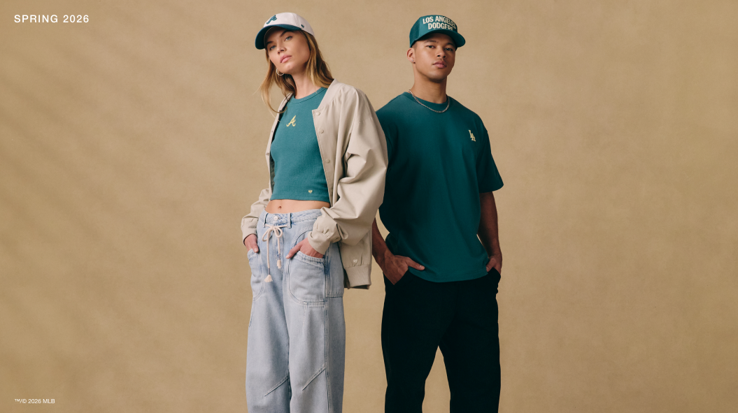 Image featuring a man in a Los Angeles Dodgers teal tee shirt and hat and a woman in a Braves tank top with a jacket on and a Braves hat in front of a tan backdrop, both in ‘47 Brand gear.
