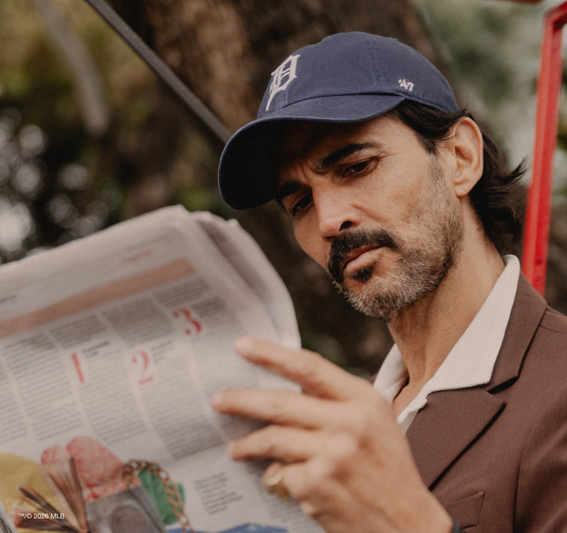 Man reading a newspaper outdoors wearing a navy Detroit Tigers Clean Up