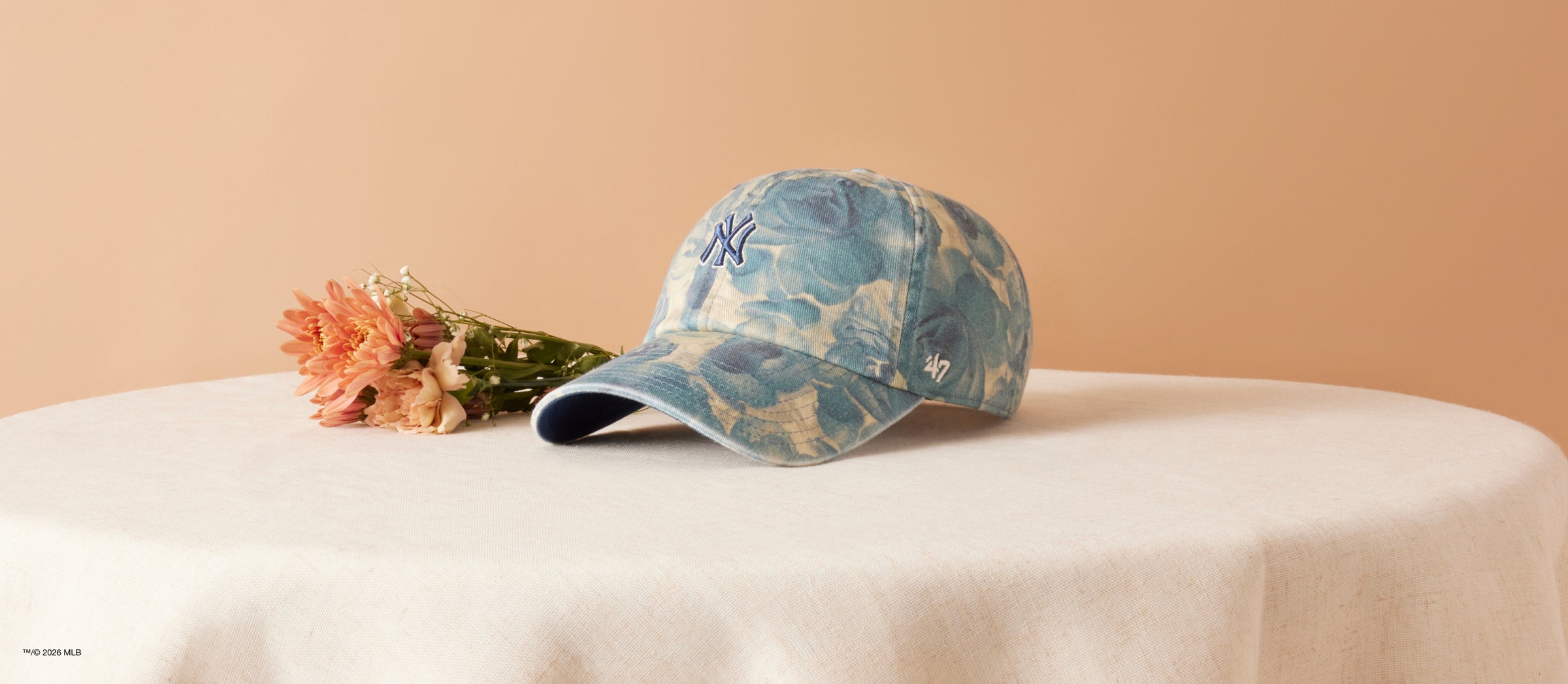 Blue cap with floral pattern on a white surface with pink flowers against a beige background