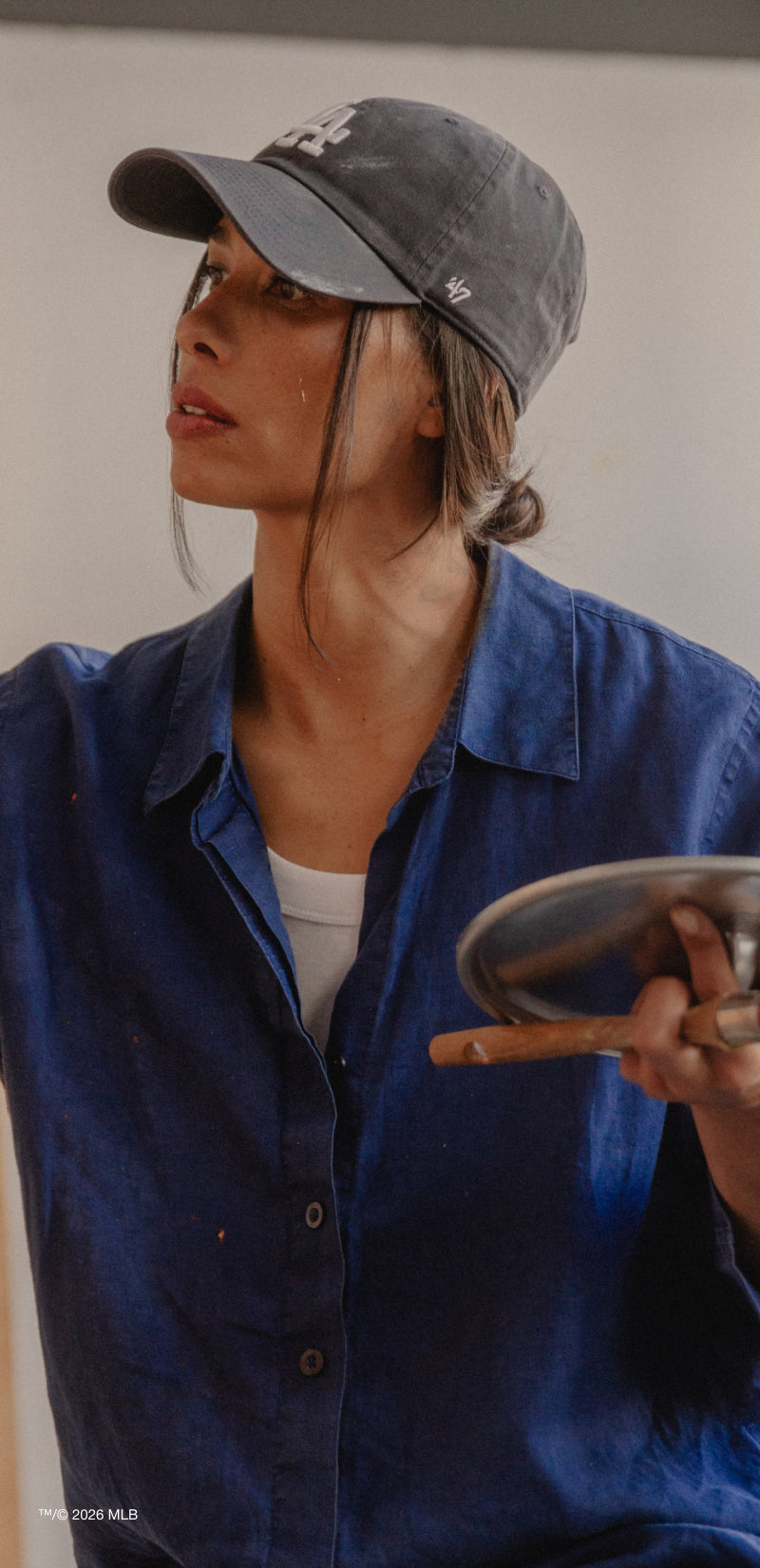 Person wearing a blue shirt and gray cap holding a paint palette against a plain background
